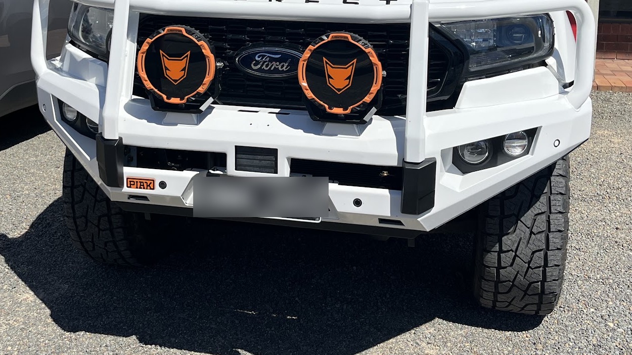 Close up of a white PIAK bull bar on a Ford Everest with a pair of orange bezel driving lights mounted